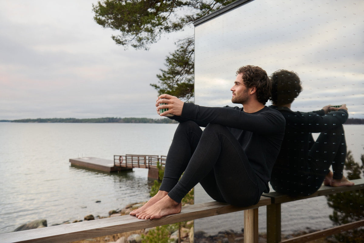 Mies istuu järven rannalla mustassa kerrastossa.